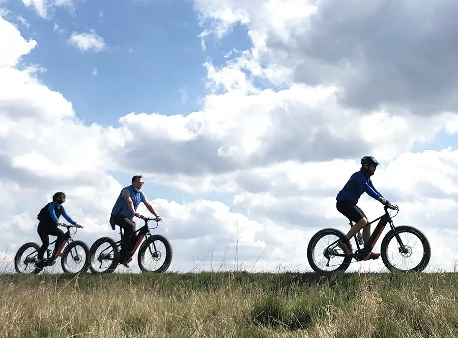 Tři cyklisté na elektrokolech na rovném horizontu Hané